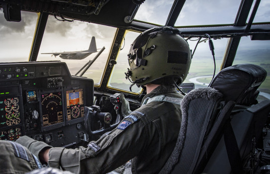 A pilot on the flight deck of a Royal New Zealand Air Force C-130H(NZ) looks out at another Hercules aircraft that's flying alongside in formation 