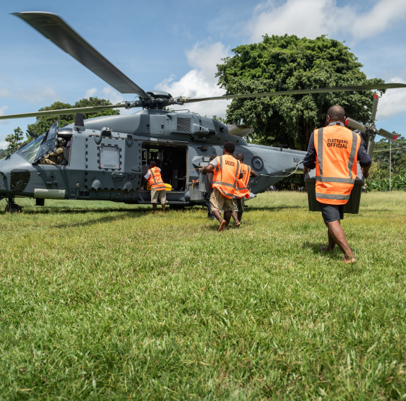 People walk on grass in high vis vests to board an NH90 helicopter on a sunny day. 