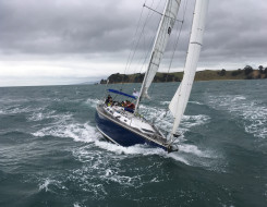 A Royal New Zealand Navy Sailing Training Craft sailing on the harbour on a grey cloudy day.