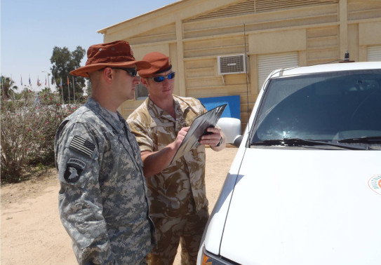 Two uniformed personnel conducting a debrief next to a vehicle. One person is pointing at a piece of paper.