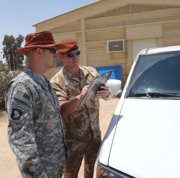 Two uniformed personnel conducting a debrief next to a vehicle. One person is pointing at a piece of paper.