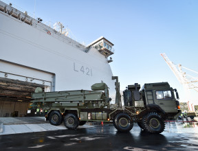 Royal New Zealand Navy's HMNSZ Canterbury berthed as a New Zealand Army MHOV drives off the ship. In the background there is blue sky and a crane as part of the port in Wellington. 