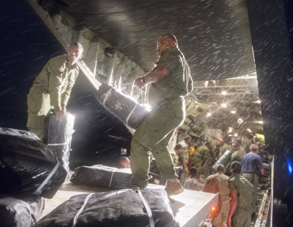 At the back of the cargo ramp of a C130 aircraft, two Fijian soldiers stand on the bed of a truck loading supplies. Behind them in the aircraft are a number of other Fijian soldiers and New Zealand Air Force personnel forming a human chain to pass parcels