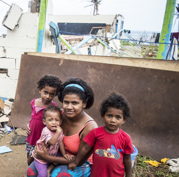 Three children and a mother pose for a photo with the damage post Cyclone Winston in the background. Further in the background you can see the beach and ocean