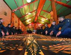 A group of sailors sit on the ground in a semi-cycle of the Royal New Zealand Navy marae with smiles on their faces and some laughing.  