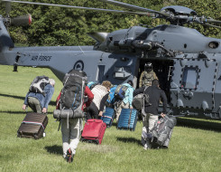 People with luggage and other bags walk toward a Royal New Zealand Air Force NH90 helicopter and Helicopter Loadmaster on the grass in Kaikōura after the earthquake