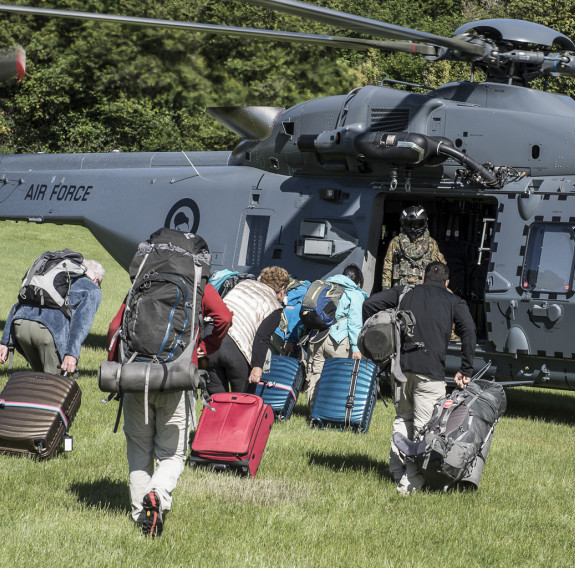 People with luggage and other bags walk toward a Royal New Zealand Air Force NH90 helicopter and Helicopter Loadmaster on the grass in Kaikōura after the earthquake