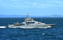 Royal New Zealand Navy's HMNZS Taupō sailing in the ocean on a nice day, blue sky in the background and some hills. 