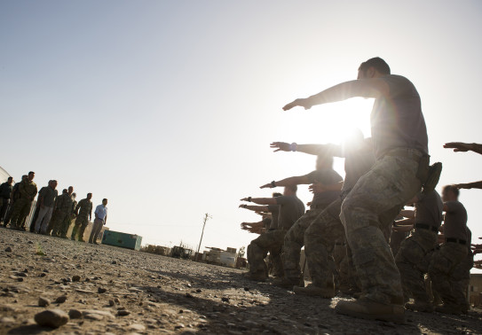 New Zealand Army soldiers perform a haka in the right of image to a group of people at Camp Taji