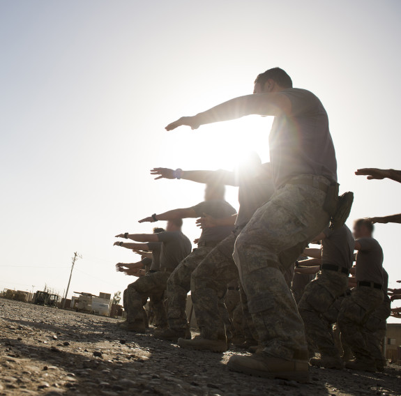 New Zealand Army soldiers perform a haka in the right of image to a group of people at Camp Taji