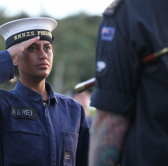 A Royal New Zealand Navy recruit salutes to another sailor (on back of them shown)