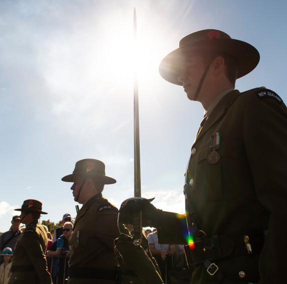 New Zealand Army soldiers as part of a Royal Guard of Honour for Anzac Day 2018. The main focus point is soldier carrying a sword and is backlit with the sun. Other soldiers are shown around and in the background you can see members of the public watching
