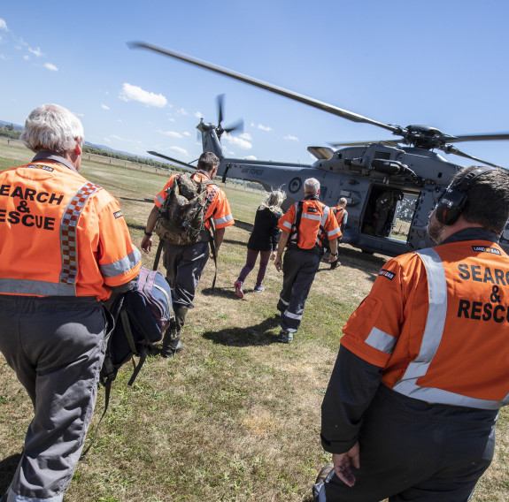 LandSAR personnel walk towards a Royal New Zealand Air Force NH90 helicopter on a nice day. 