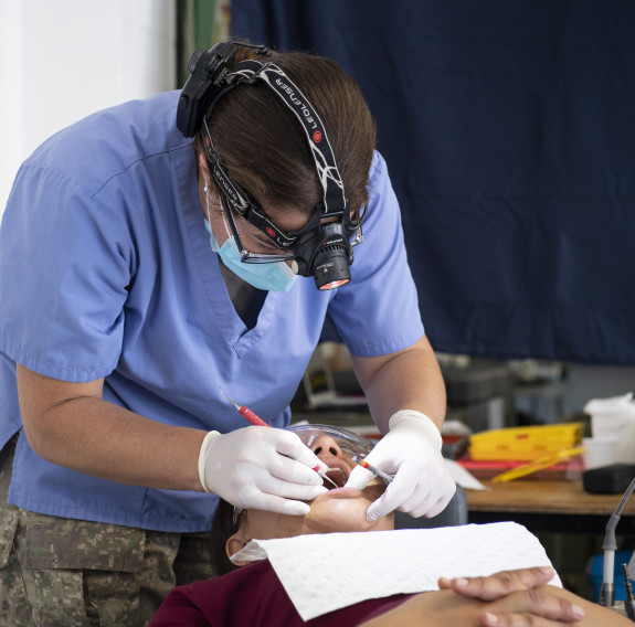 An NZDF dentist working on a patients mouth using a head torch. 