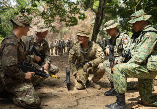 A group of military personnel either site or with one leg up in a semi-cycle talking and laughing.