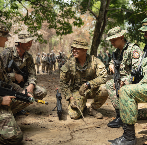 A group of military personnel either site or with one leg up in a semi-cycle talking and laughing.