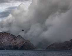 A SH-2G(I) Seasprite Helicopter flies in the air near the Whaakari/White Island. In the image you can see smoke erupting from the volcano