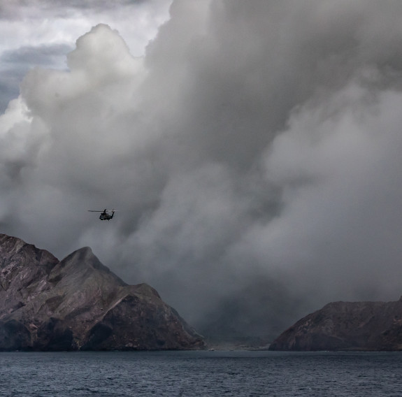 A SH-2G(I) Seasprite Helicopter flies in the air near the Whaakari/White Island. In the image you can see smoke erupting from the volcano