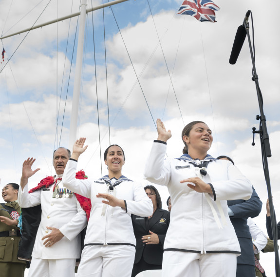 NZDF personnel perform and sing a waiata near a flag mask. Three Royal New Zealand Navy sailors are in the foreground. 