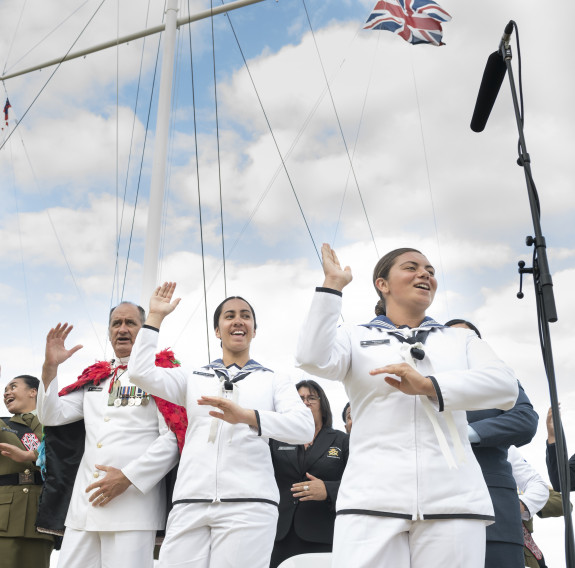 NZDF personnel perform and sing a waiata near a flag mask. Three Royal New Zealand Navy sailors are in the foreground. 