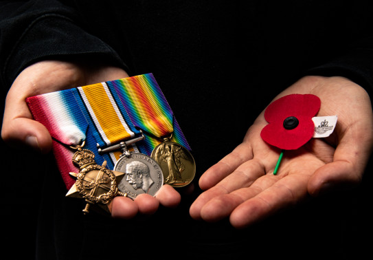 Two hands holding some service medals on the left and an RSA Poppy in the other hand (right side) 