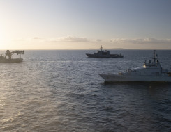 Three Royal New Zealand Navy ships sailing in the ocean HMNZS Otago, HMNZS Hawea and HMNZS Manawanui on a nice evening. There is some sun flare to the left of the image