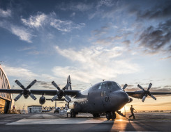 A Royal New Zealand Air Force C-130H(NZ) Hercules aircraft on the flight line at Base Auckland early in the morning as the sun is coming up. One of the Air Loadmasters is walking off the aircraft. In the background to the left you can see the aircraft han