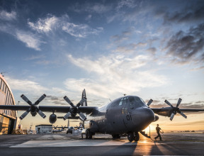 A Royal New Zealand Air Force C-130H(NZ) Hercules aircraft on the flight line at Base Auckland early in the morning as the sun is coming up. One of the Air Loadmasters is walking off the aircraft. In the background to the left you can see the aircraft han