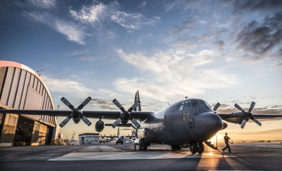 A Royal New Zealand Air Force C-130H(NZ) Hercules aircraft on the flight line at Base Auckland early in the morning as the sun is coming up. One of the Air Loadmasters is walking off the aircraft. In the background to the left you can see the aircraft han