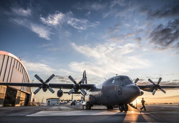 A Royal New Zealand Air Force C-130H(NZ) Hercules aircraft on the flight line at Base Auckland early in the morning as the sun is coming up. One of the Air Loadmasters is walking off the aircraft. In the background to the left you can see the aircraft han