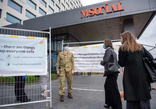 A New Zealand Army soldier at the gate of one of the COVID-19 Managed Isolation Facilities. Two people meet the soldier at the gate.