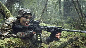 A New Zealand Army soldier in the New Zealand bush with MARS-L weapon. The area is all wet and very green. The soldier has his mouth open as he yells a command. 