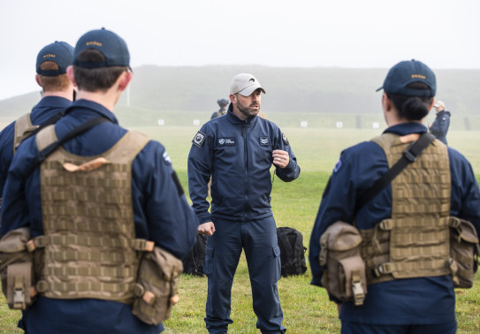 A Royal New Zealand Air Force airman speaks to a group of airmen during training at the range. The day is very misty and wet.