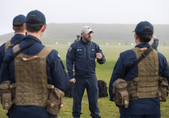 A Royal New Zealand Air Force airman speaks to a group of airmen during training at the range. The day is very misty and wet.