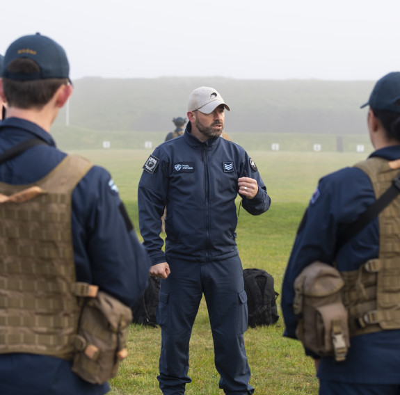 A Royal New Zealand Air Force airman speaks to a group of airmen during training at the range. The day is very misty and wet.