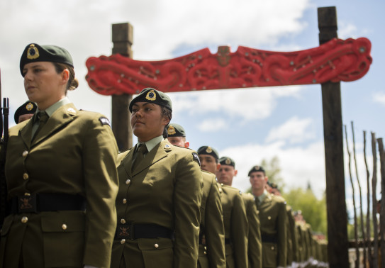New Zealand Army soldiers walk under an arch made of Māori carvings