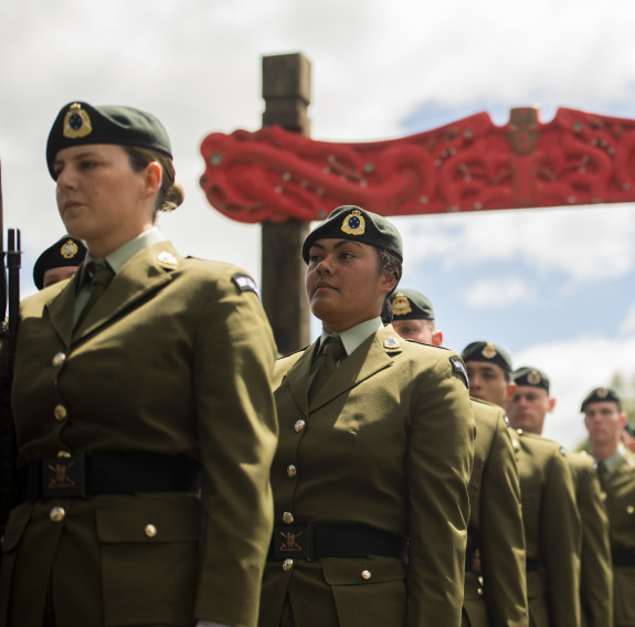 New Zealand Army soldiers walk under an arch made of Māori carvings