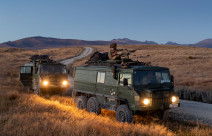 Two New Zealand Light Operational Vehicle (NZLOV) and soldiers in the evening light with their lights on. They are parked on the side of the gravel road and in the background you can see hills around the Waiouru Military Training Area