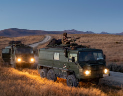 Two New Zealand Light Operational Vehicle (NZLOV) and soldiers in the evening light with their lights on. They are parked on the side of the gravel road and in the background you can see hills around the Waiouru Military Training Area