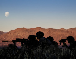 New Zealand Army soldiers using the Designated Marksman Weapon (DMW). The soldiers are silhouetted with the mountain range in the background lit up