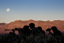 New Zealand Army soldiers using the Designated Marksman Weapon (DMW). The soldiers are silhouetted with the mountain range in the background lit up