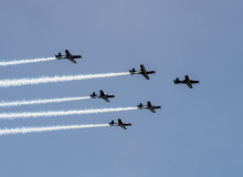 The Royal New Zealand Air Force Black Falcons fly in formation (five T-6C Texan II aircraft). The sky is blue.