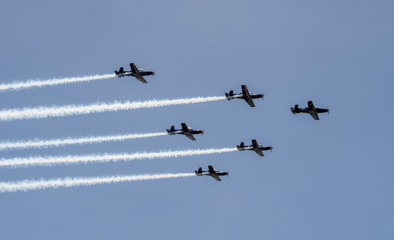 The Royal New Zealand Air Force Black Falcons fly in formation (five T-6C Texan II aircraft). The sky is blue.