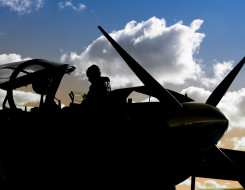 A Royal New Zealand Air Force pilot about to get in a T-6C Texan II aircraft. The pilot and the aircraft is silhouetted in the image. The sky is blue with a bit of cloud. 