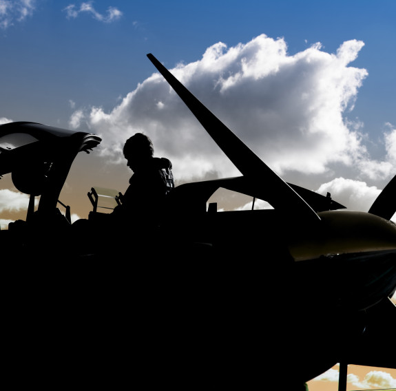 A Royal New Zealand Air Force pilot about to get in a T-6C Texan II aircraft. The pilot and the aircraft is silhouetted in the image. The sky is blue with a bit of cloud. 