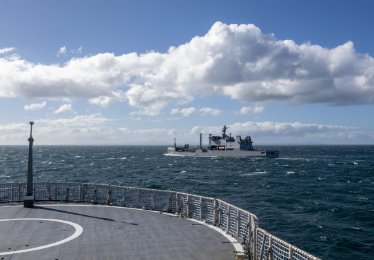 HMNZS Aotearoa transits alongside HMNZS Manawanui sails in the Hauraki Gulf on a sunny day with some cloud in the sky
