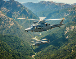 Two A109 helicopters fly over the mountain range. 
