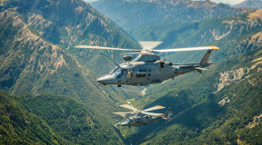 Two A109 helicopters fly over the mountain range. 