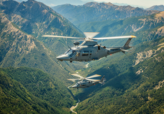 Two A109 helicopters fly over the mountain range. 