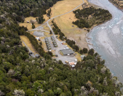 An aerial view of Dip Flat. This camp consists of one large building, 14 cabins and four other smaller buildings. The camp is located next to a river on the right and otherwise is surrounded by trees.
